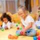adorable multicultural kids playing with colored balls on floor in kindergarten